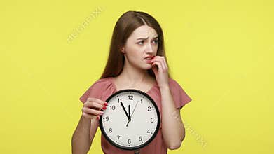 Girl holding big wall clock, biting finger nails.