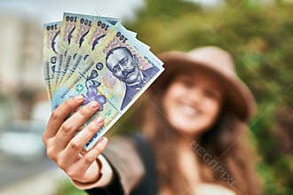 Young hispanic tourist woman smiling happy holding romania lei banknotes at the city