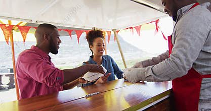 African american man wearing apron serving burgers and fries to a couple at the food truck