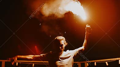 Fanatical man burning light on roof. Aggressive protester waving torch outdoors.