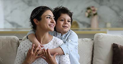 Young Indian mother and preschooler son hugging looking into distance