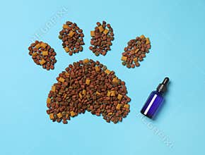 Tincture in glass bottle near pet footprint of pelleted dry food on light blue background, flat lay