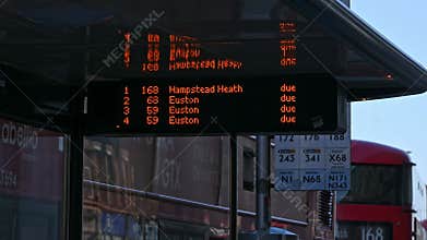 A close up of a sign in a bus stop saying which buses are due as the Red London Double Decker Buses which are due on the sign