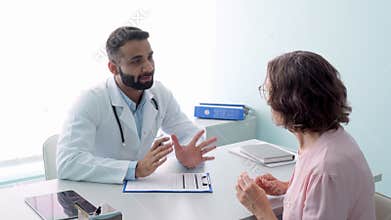 Smiling Indian doctor having appointment with female patient in hospital.