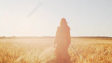 Beautiful young woman walks across the field and touches rye with her hand. Girl in the rays of the sunset. Freedom and
