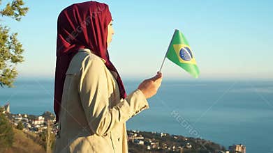 Muslim woman in hijab with flag of Brazil. Immigration, religion or travel concept. Background of the sea and beautiful