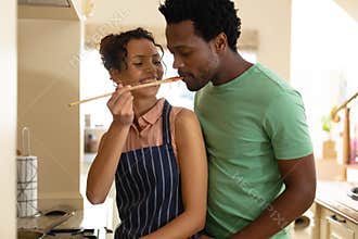 Smiling young biracial woman tasting food to african american boyfriend while cooking at home