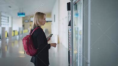 An attractive young woman pays for her coffee at the vending machine.