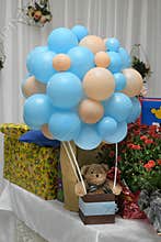 Teddy bear with gift box sits on background children`s jewelry with glowing lights, birthday garland, red flowers