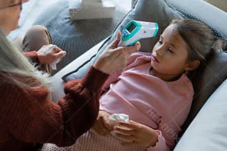 Grandmother taking care of her ill grandchild lying on sofa