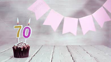 Birthday number 70. Festive background for a girl or woman with a muffin and candles burning pink in pastel colors with decoration