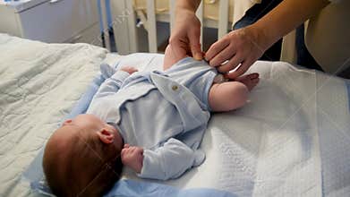 Closeup of mother changing diapers and dressing her little baby son on bed at night.