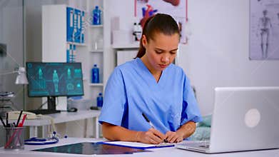 Medical assistant typing on laptop and taking notes on clipboard