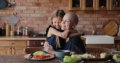 Sick bald woman embrace adorable little daughter in kitchen