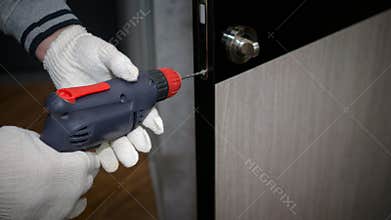The foreman carries out repair work in the apartment  drills the door lock  the man repairs the interior door.
