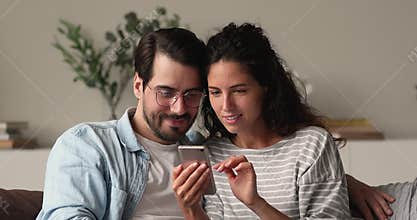 Couple sit on couch holding smartphone celebrate online betting victory