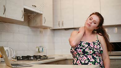 Portrait of the tired woman with weight problems doing self-massage in the kitchen.