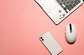 Minimal flat lay photo with a silver grey laptop computer, modern smartphone, white plastic mouse, and wireless earphones on a