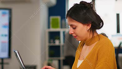 Young woman working at laptop sitting at desk in busy financial startup company