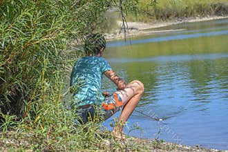 Boy Squatting Behind Bushes and Fishing in Lake