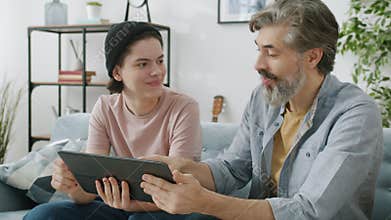 Slow motion of teenage boy and father using tablet chatting then doing high-five