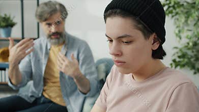 Caring dad talking to stubborn teenager who is ignoring parent feeling offended sitting at home