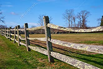 An old split-rail fence with green lichen borders a field.