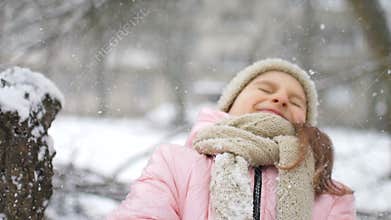 Winter portrait of a kid girl in pink coat wearing beige hat and mittens playing outdoor in snowy winter forest and