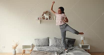 Overjoyed millennial woman dancing to music on bed.