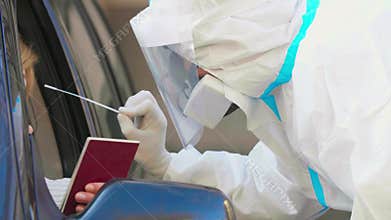 Woman showing passports, medical worker in PPE performing drive-thru COVID-19 test