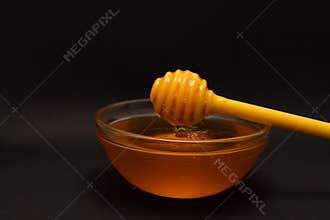 Yellow spoon of honey dipped in a jar of honey on a black background. Honey dripping around, nice and inviting photos