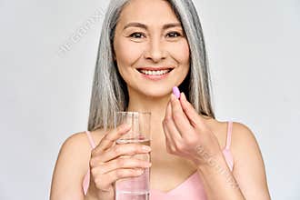Portrait of happy smiling mid aged Asian woman taking pills  on white.