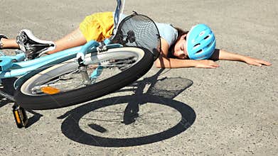 Young girl fallen of a bicycle laying down beside her bike unconscious on paved road