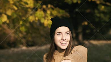 Beautiful girl poses with smile under the striking ray of the sun in autumn park