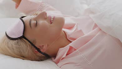 Beautiful woman wearing sleep mask waking up in bed in the morning