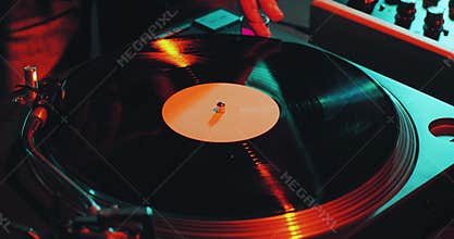 Deejay spinning vinyl musical record on turntable during dj rave, close-up. Nightlife and music
