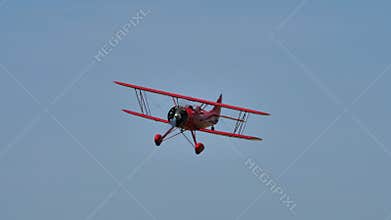 Vintage red biplane from 1930 in flight in a blue summer sky without clouds