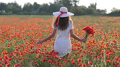 Young brunette woman in white dress stands in the middle of the field of poppies. Charming lady with incredible smile