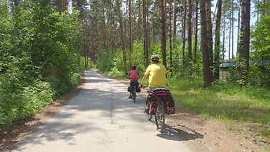 Two young men with backpacks ride bicycles along the road.