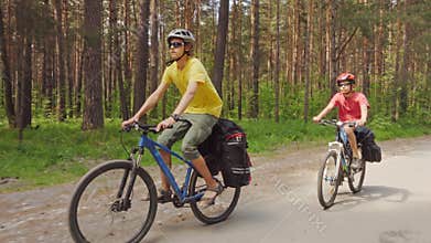 Two young men with backpacks ride bicycles along the road.