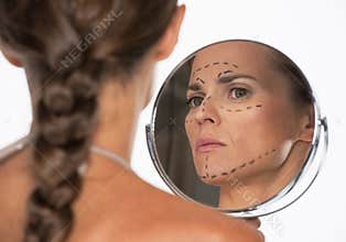 Woman with plastic surgery marks on face looking in mirror