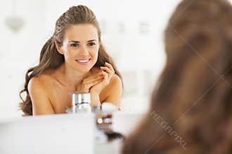 Portrait of happy young woman looking in mirror in bathroom
