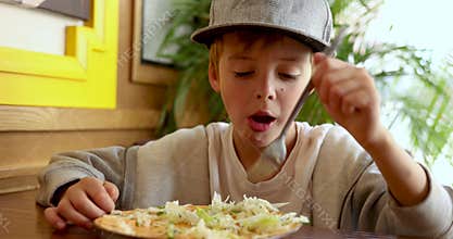 Boy eating salad with appetite in restaurant