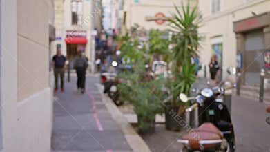 Blurred pedestrians walk along a lively street in marseilles, france, with vivid greenery and scooters adding to the bustling