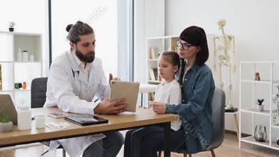 Caucasian doctor discusses health with mother and daughter in clinic
