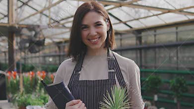 Portrait of a beautiful young woman in a greenhouse. A woman holds a succulents and notepad in her hands, with many