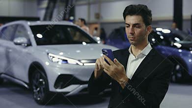 Man Buyer Standing in Car Dealership and Browsing the Online Auto Store, Thinking About Buying Car.