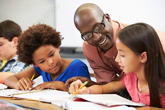 Teacher Helping Pupils Studying At Desks In Classroom
