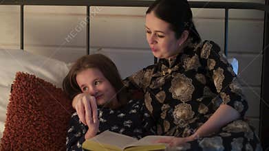 An adopted daughter reading bible with her mum on a bed. Concept of religious christians family. Read the fairy tales