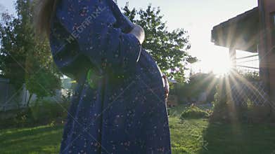 Beautiful pregnant woman enjoying fresh air at sunset rays on the backyard